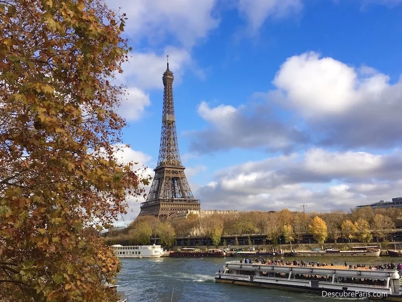 Torre eiffel en un fondo de cielo azul con nubes blancas, y enmarcado en arboles de otoño