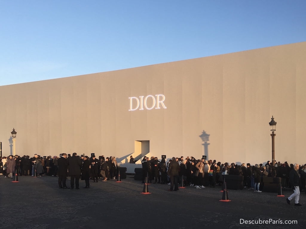 Vista exterior del desfile de Dior Homme se ve la fachada blanca con las letras de la marca y la gente esperando afuera