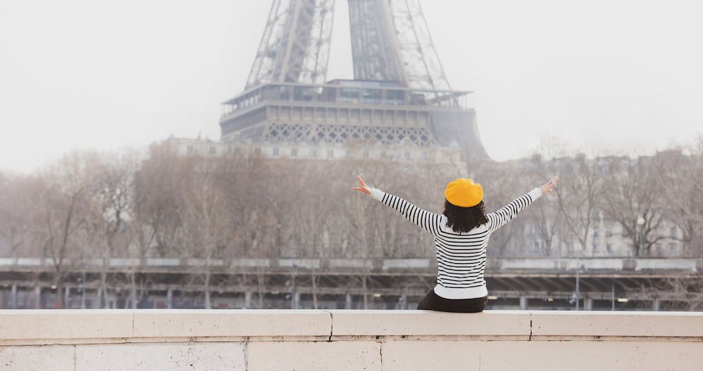 mujer mirando a la torre eiffel con los brazos abiertos y vestida con una marinera y una boina francesa